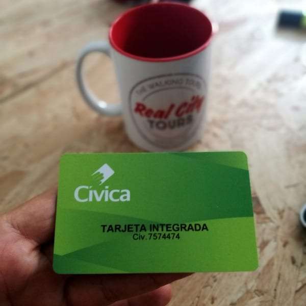 Green Cívica integrated transit card held in front of a Real City Tours coffee mug on a wooden surface