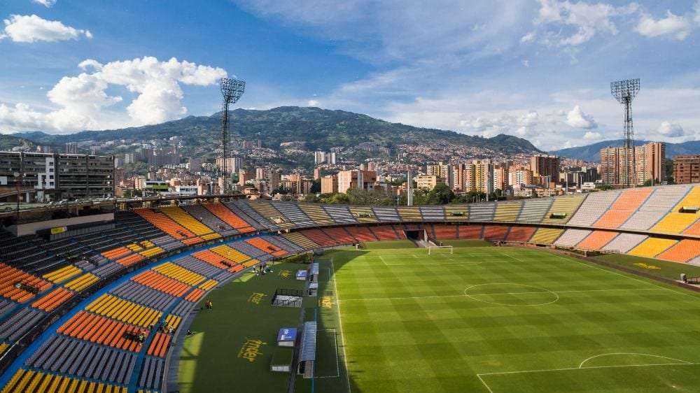 Aerial view of Estadio Atanasio Girardot in Medellín with colorful orange and yellow seats and Andes mountains behind