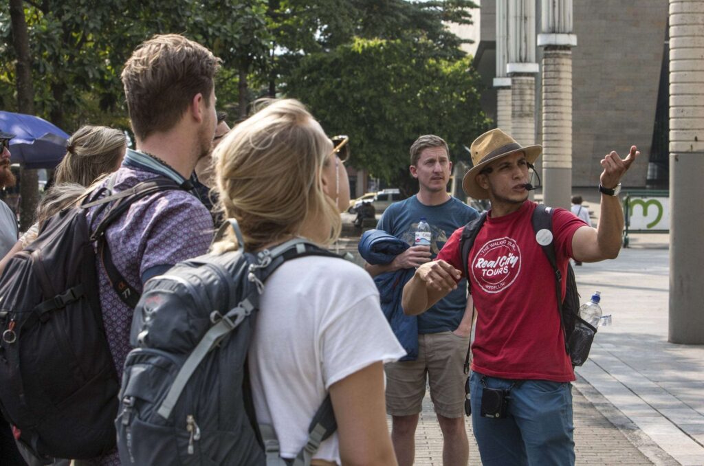Real City Tours guide wearing a red shirt speaking to backpacker tourists during a free walking tour of Medellín