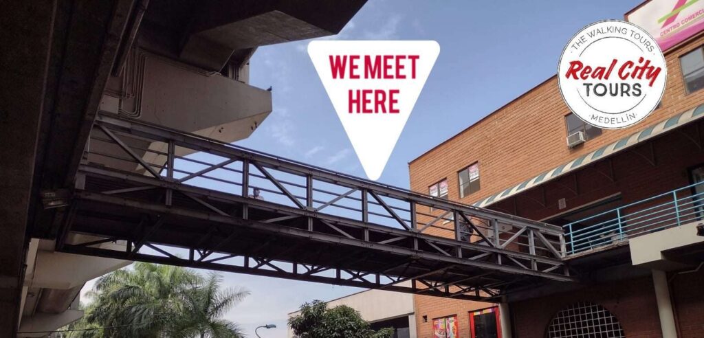 We Meet Here graphic pedestrian bridge near Medellín metro station marking the Real City Tours free tour meeting point