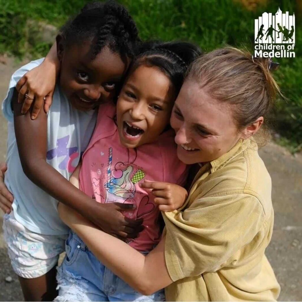 Volunteer with Children of Medellín organization hugging two laughing local children outdoors