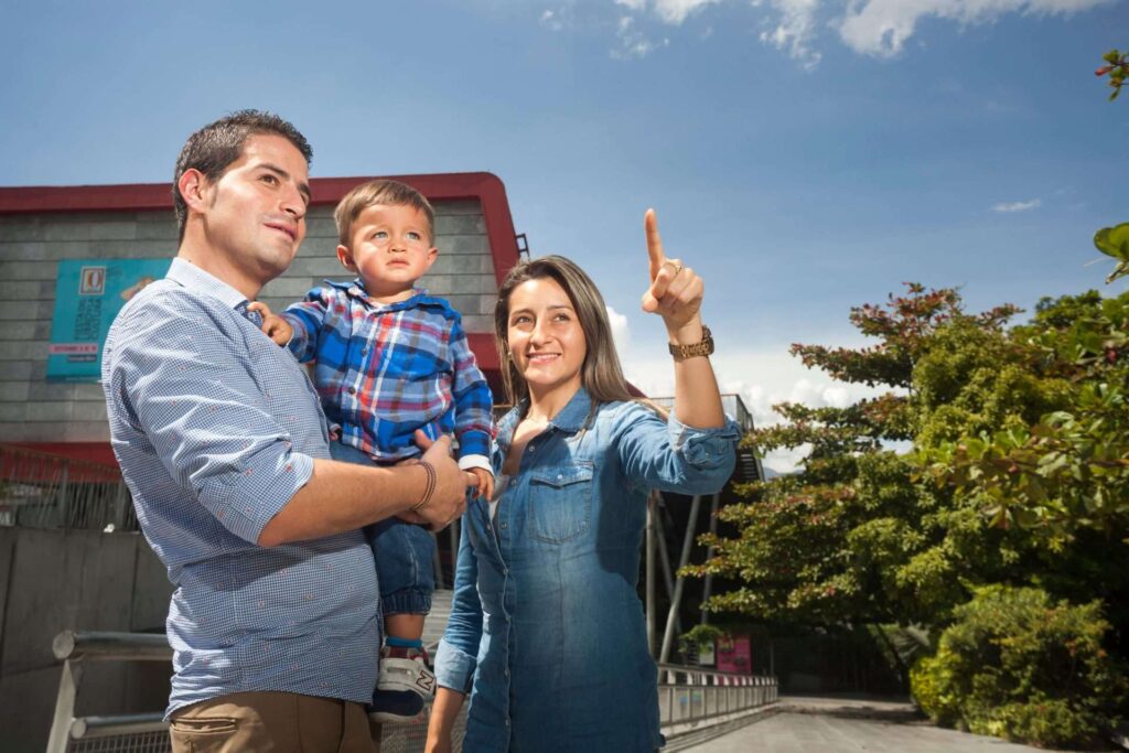 Parents holding toddler pointing toward Parque Explora building exterior in Medellín Colombia