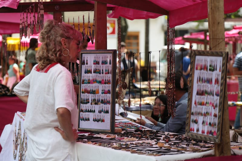 Woman browsing colorful earrings and necklaces at an artisan jewelry market stall in Medellín
