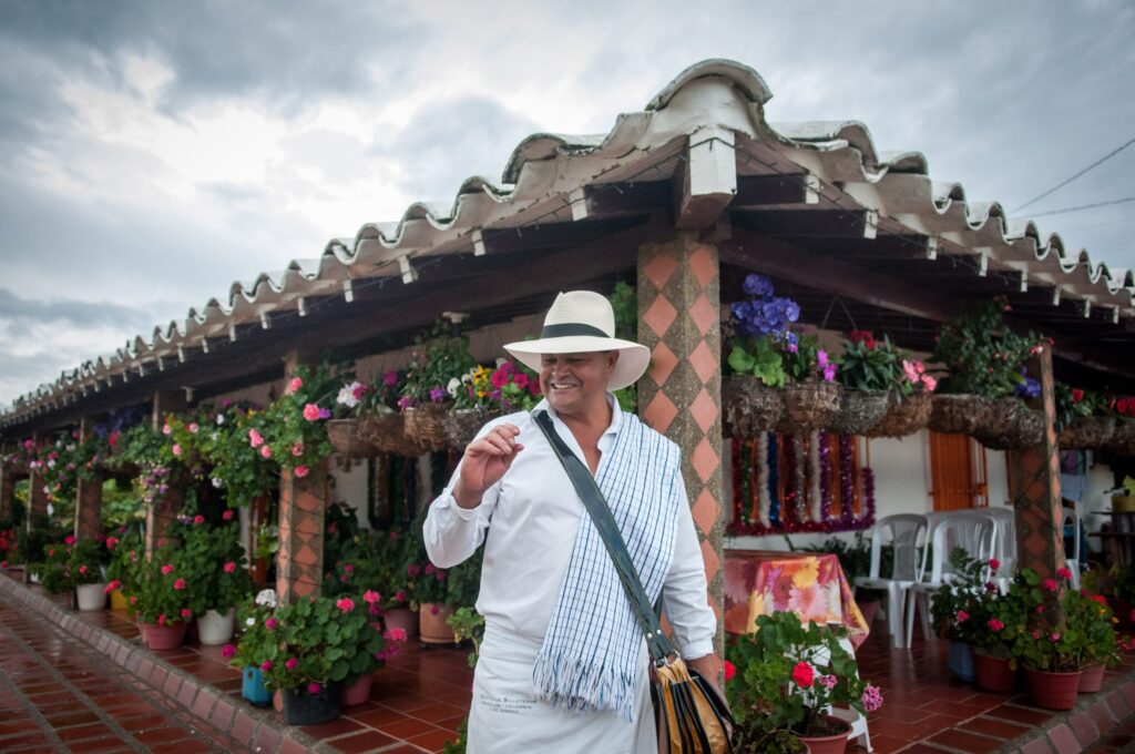 Smiling man in Panama hat standing before a flower-adorned traditional Colombian restaurant terrace
