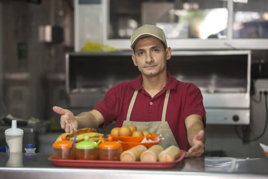 Smiling local restaurant owner presenting a tray of Colombian street food including pandebono and empanadas