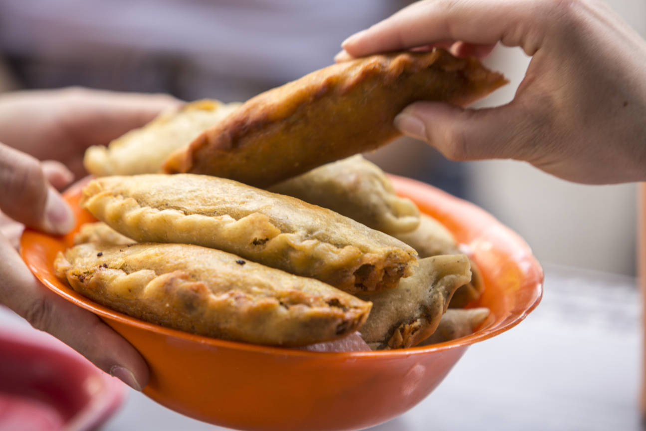 Hand picking a Colombian empanada from an orange bowl filled with fried pastries on a food tour