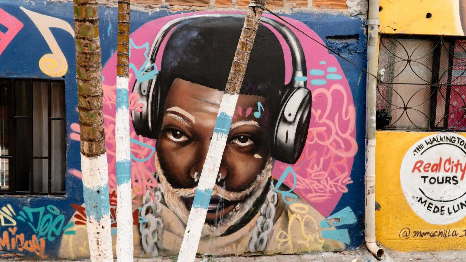 Colorful street art mural of a young man with headphones in Comuna 4 with Real City Tours logo