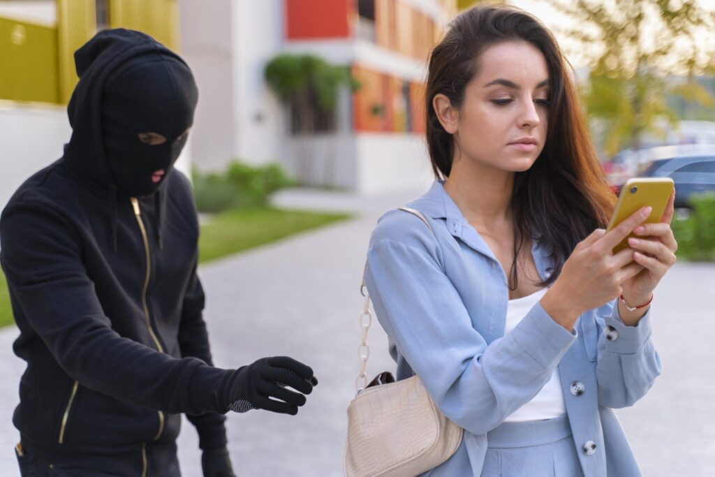 Illustration of pickpocket risk showing masked thief approaching a distracted woman looking at her phone