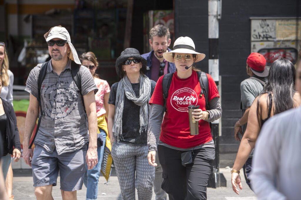 Real City Tours female guide in red shirt and Panama hat leading tourists through Medellín street