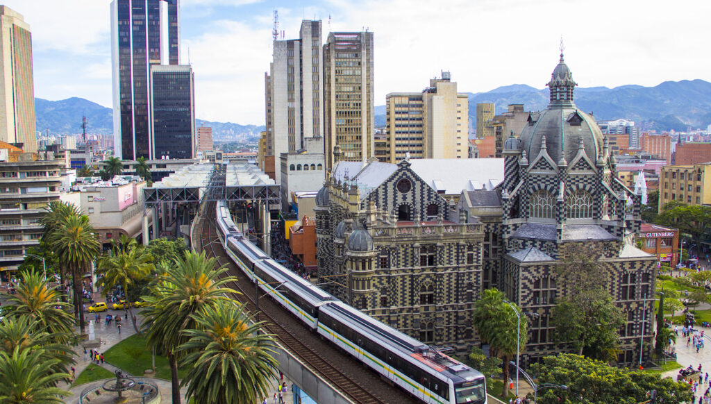 Medellín Metro train passing alongside the ornate Palacio de la Cultura Rafael Uribe Uribe with palm trees