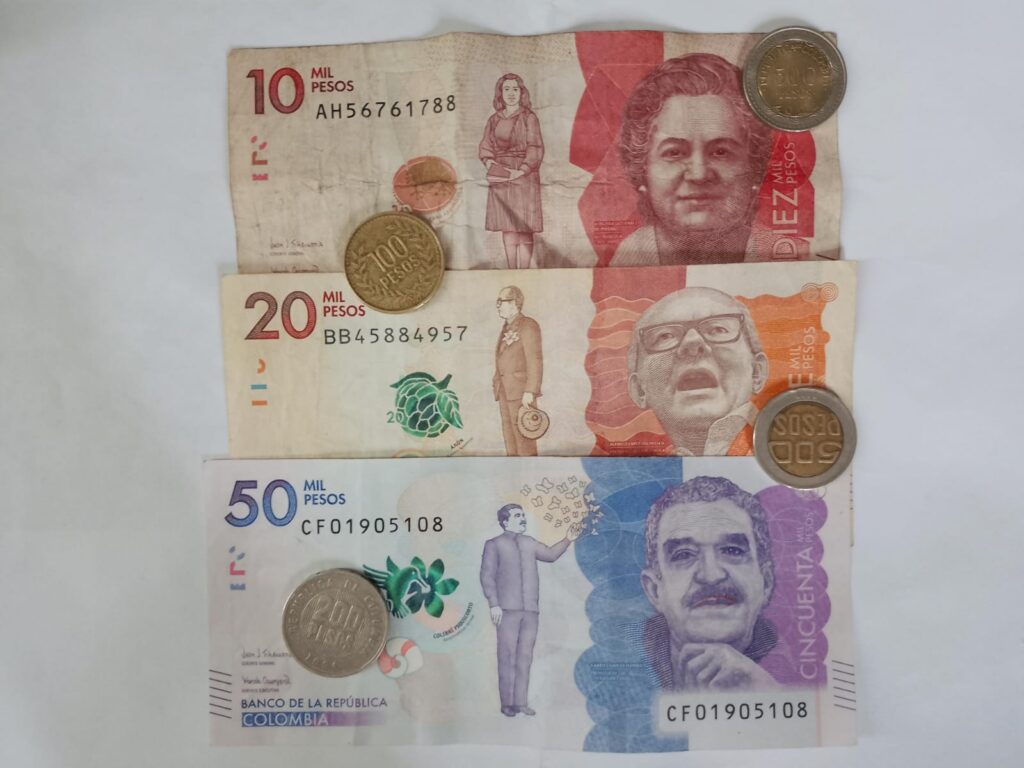 Colombian peso banknotes of 10,000 20,000 and 50,000 pesos with coins displayed on a white surface
