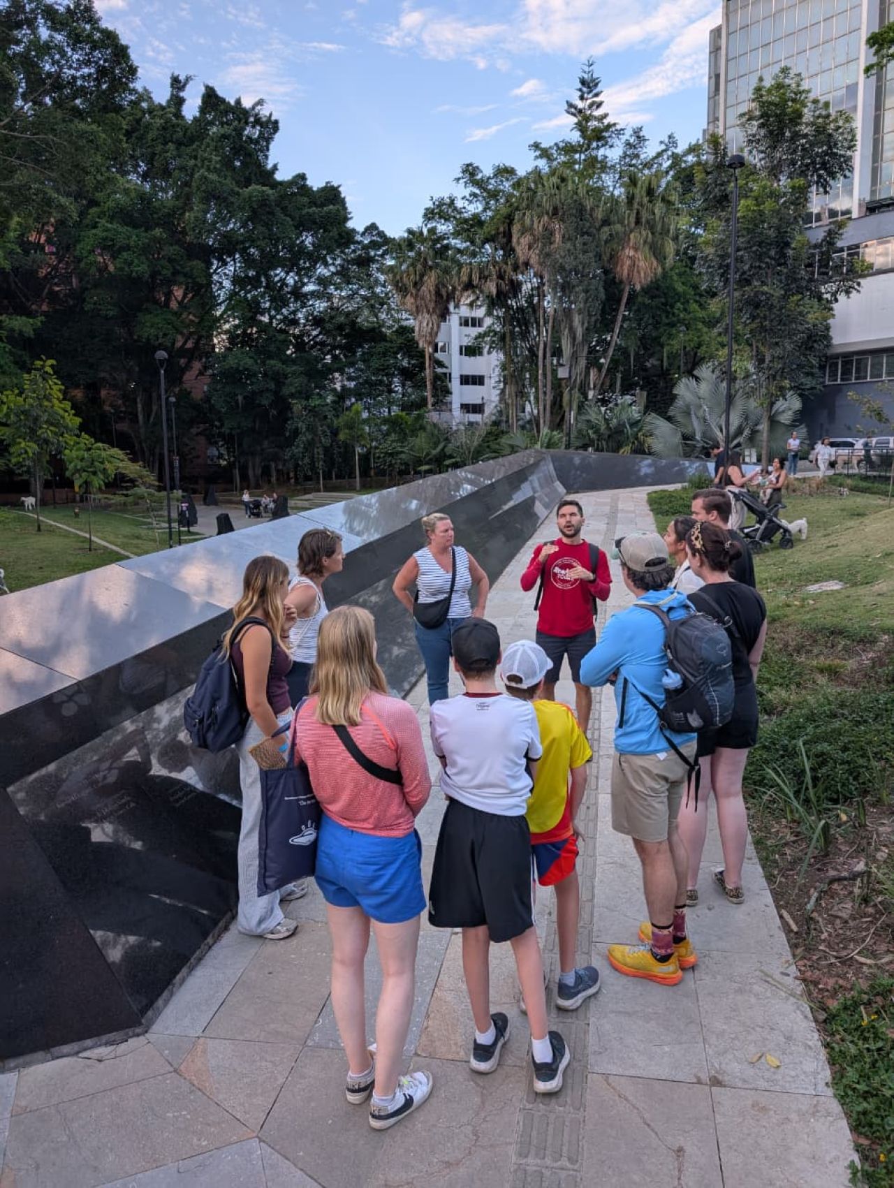 Real City Tours guide in red shirt explaining a historic memorial monument to a tourist group in Medellín
