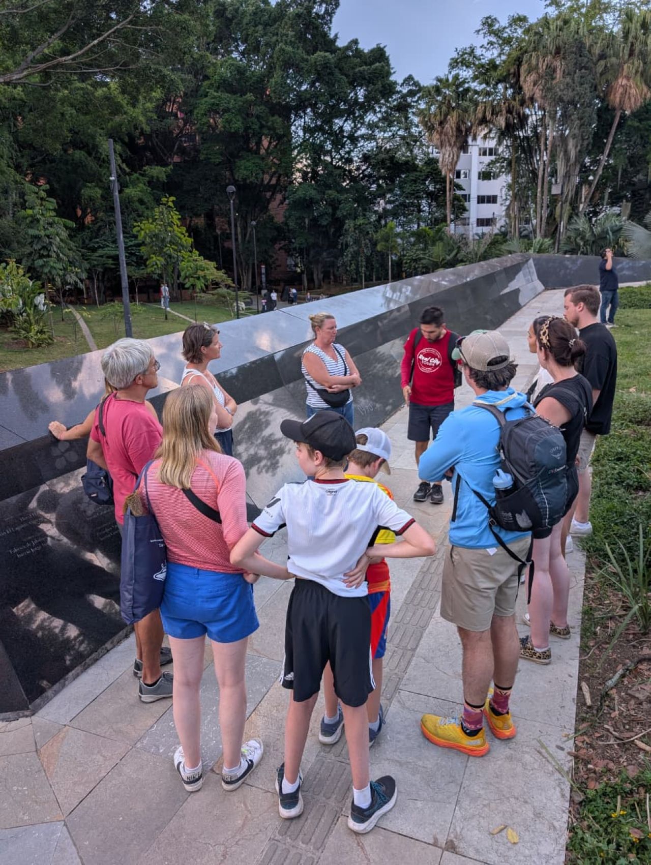 Real City Tours tourist group gathered at a dark reflective memorial wall during a Medellín walking tour