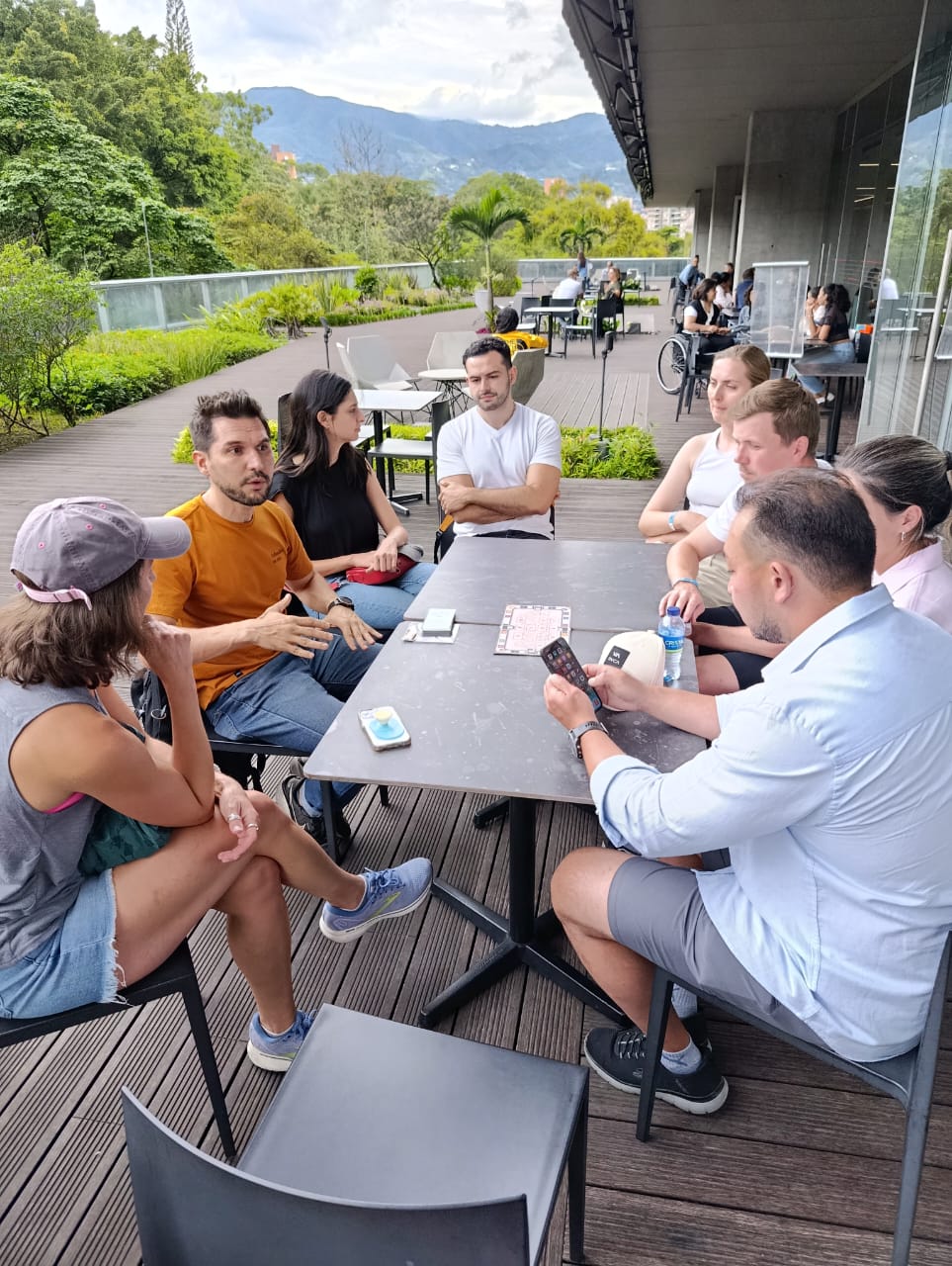 Tour group and guide seated at an outdoor terrace table discussing Medellín with mountain views behind